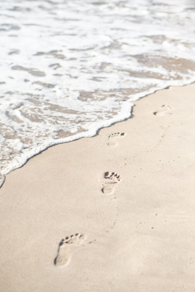 Ocean wave washing away footprints in the sand.
